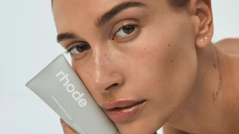 A close-up of a model holding a Rhode skincare tube against her cheek